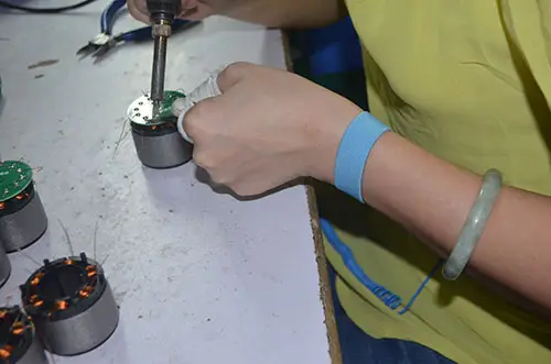 Eine Hand mit ESD-Armband, die einen Stator während des Schweißens auf elektrostatische Entladung prüft.